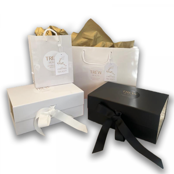 Selection of Trew beauty gift box options including a small white bag, large white bag, white box with ribbon and black box with ribbon, complete with tissue paper and branding